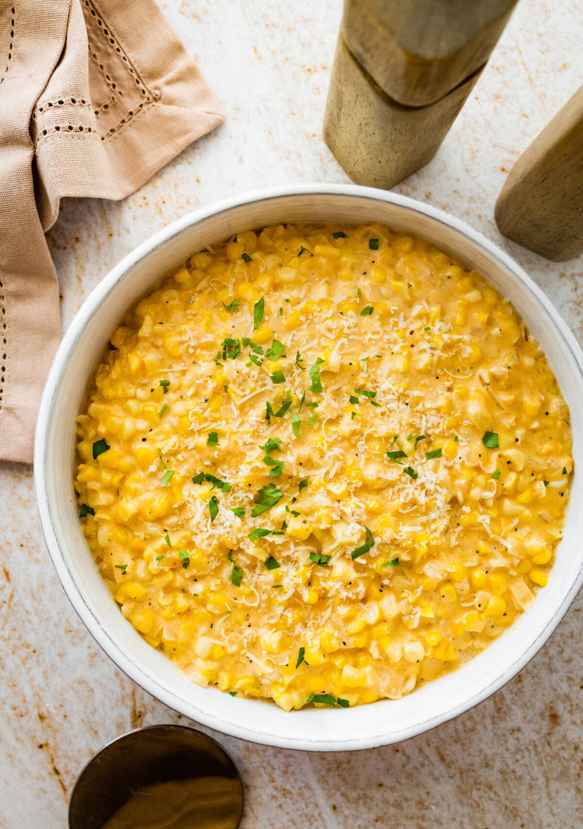 creamed corn recipe in a white bowl with a little parsley on top and extra cheese.