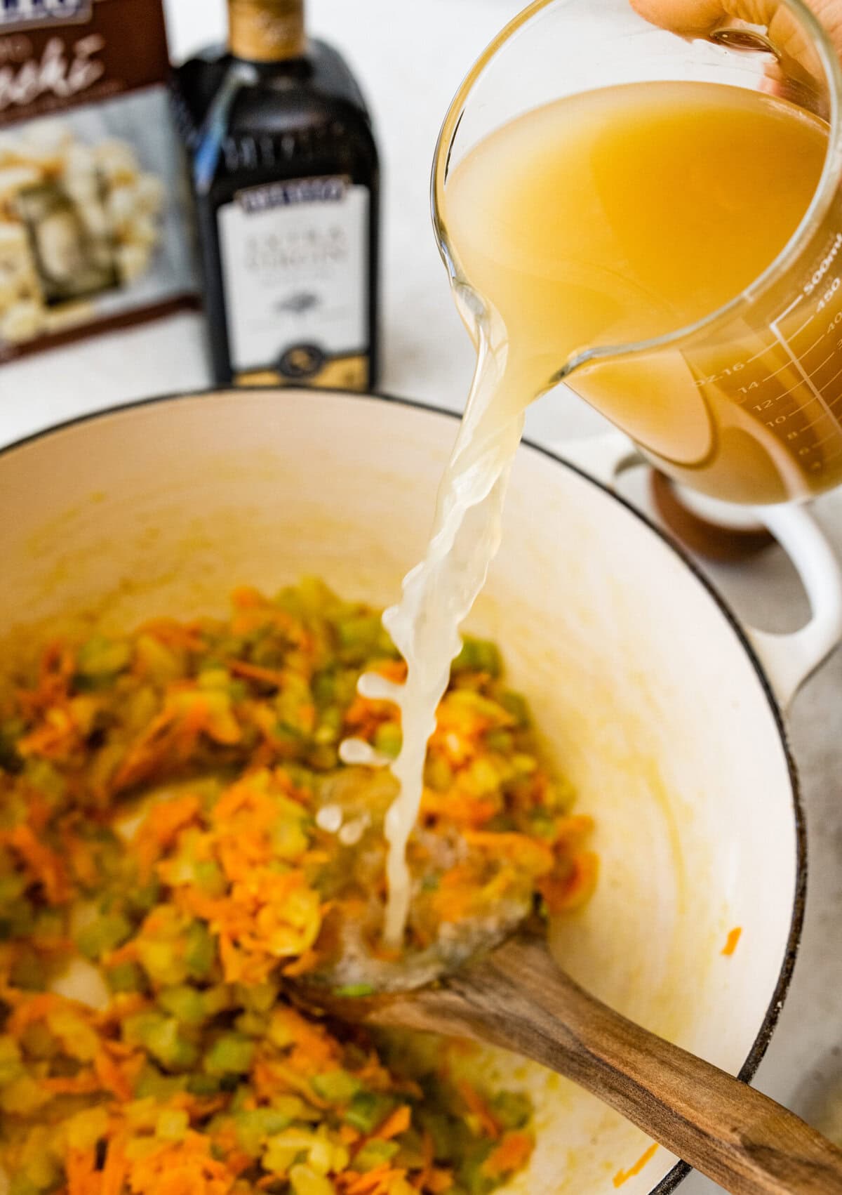 pouring broth into the soup pot with cooked veggies.