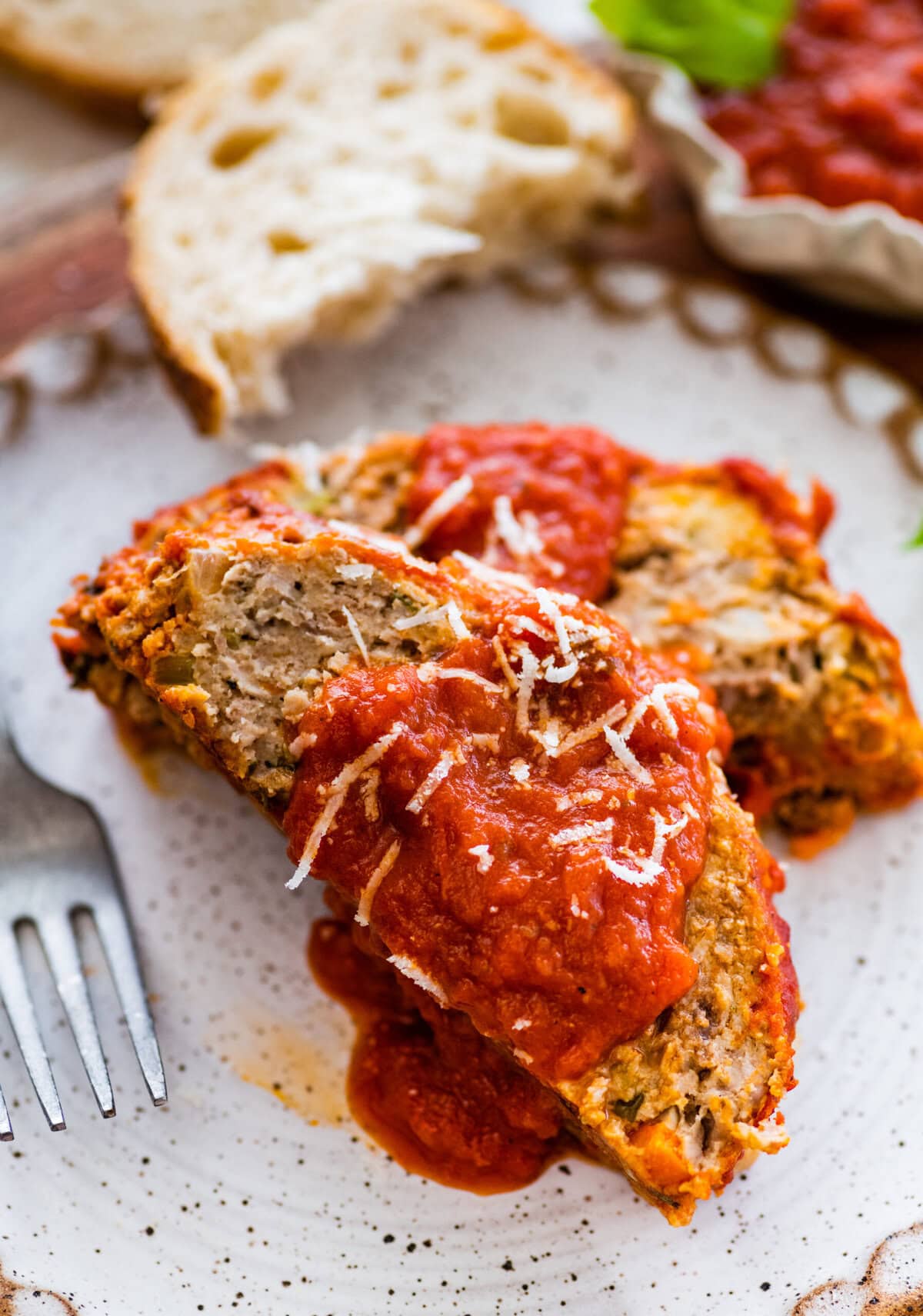 two slices of Italian meatloaf on a plate with extra sauce on top and bread on the side.