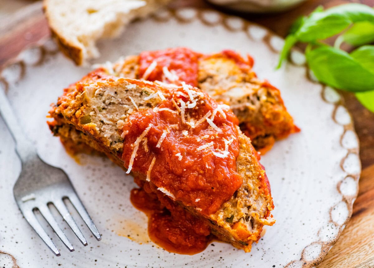 two slices of Italian meatloaf on a plate with extra sauce on top and bread on the side.