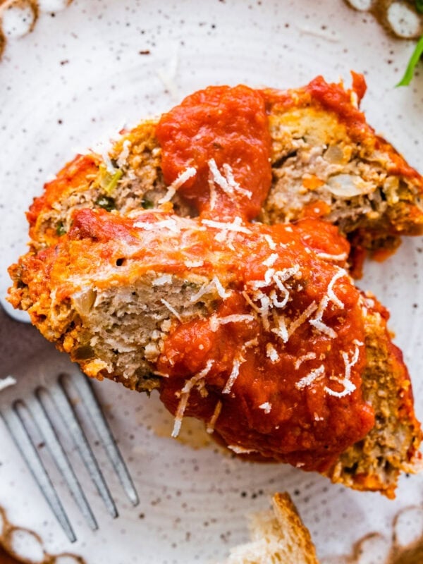 two slices of Italian meatloaf on a plate with extra sauce on top and bread on the side.