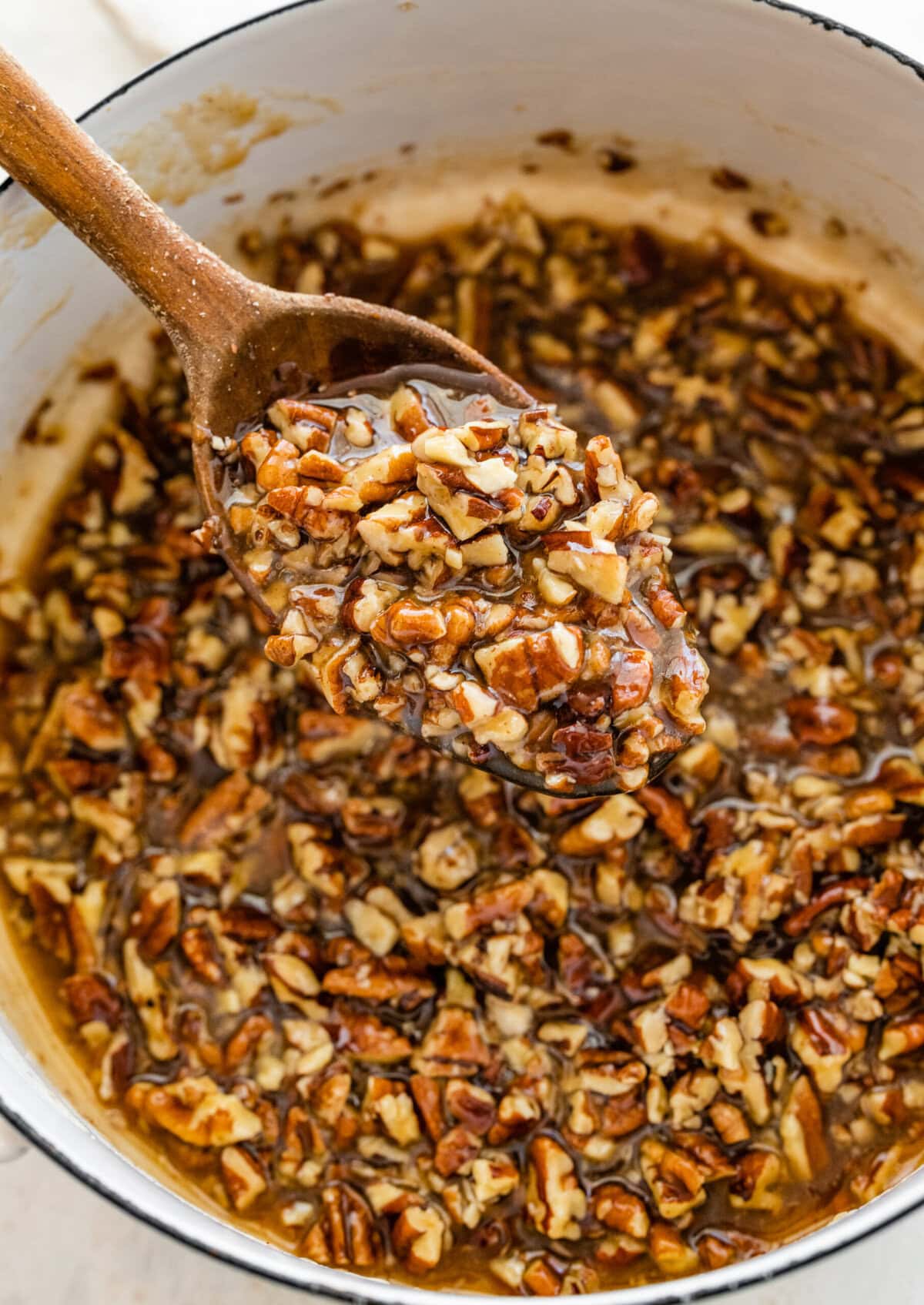 gooey pecan pie topping in a bowl with a wooden spoon.