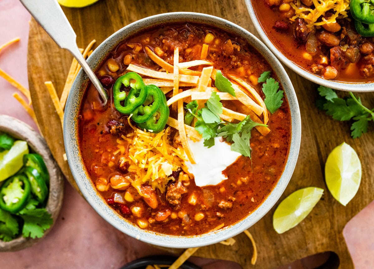 a bowl of taco soup with cheddar cheese, sour cream, and jalapenos. Spoon in the bowl.