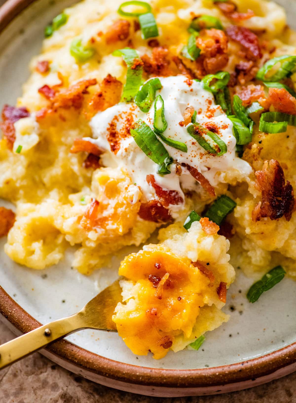 plate with a serving of twice baked potato casserole topped with sour cream and a fork to eat it with.