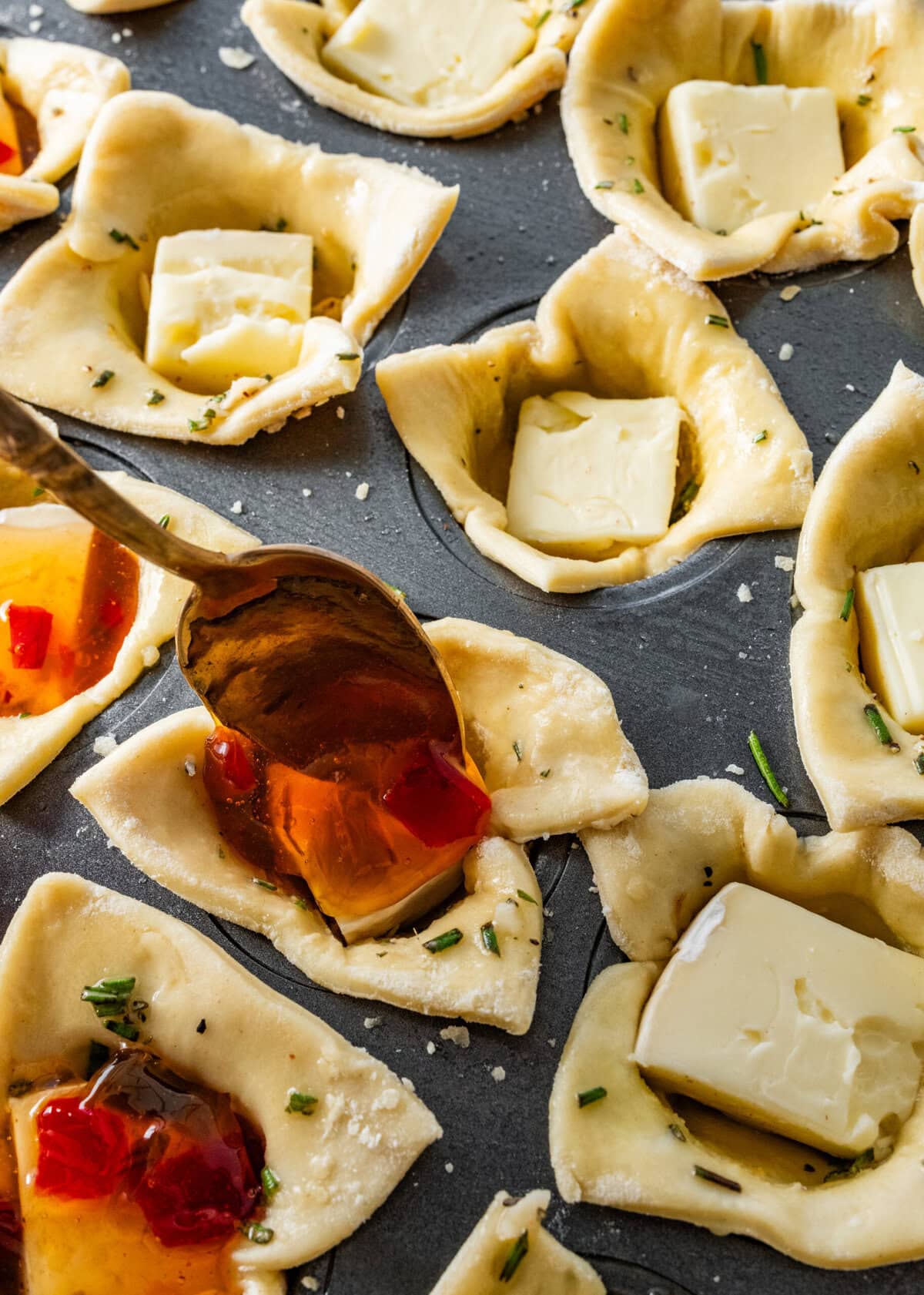 puff pastry bites in muffin tins. A spoon adding hot pepper jelly on top.