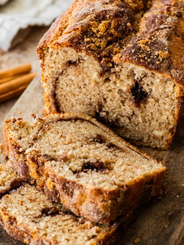 slices of moist cinnamon swirl bread on a wooden cutting board with loaf in the background.