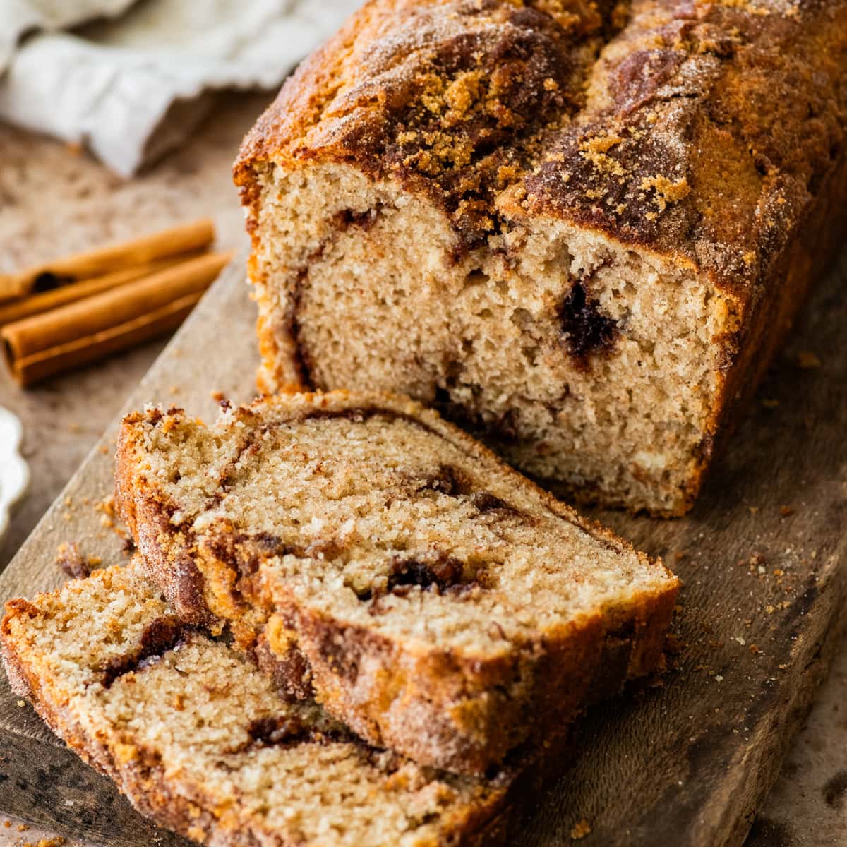 slices of moist cinnamon swirl bread on a wooden cutting board with loaf in the background.