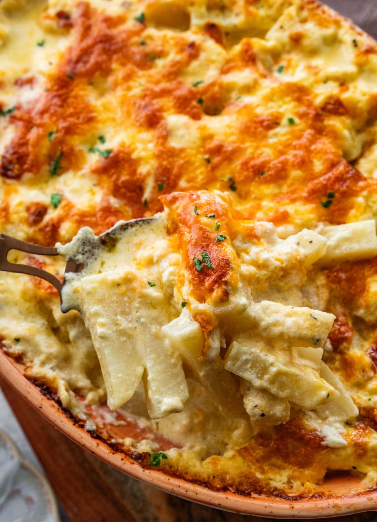 Serving spoon lifting a portion of the cheesy potatoes.