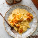 cheesy potatoes on a white plate with lots of cheesy sauce and a fork ready to eat.