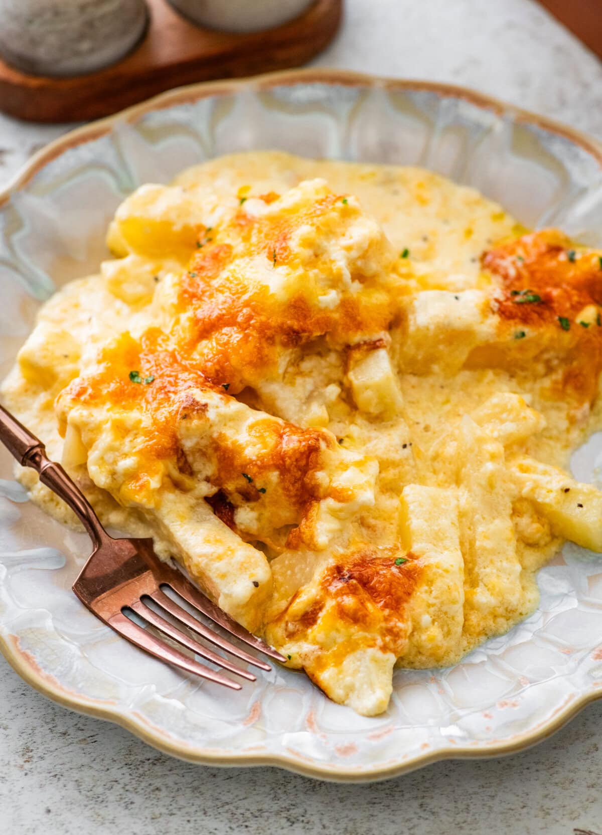 cheesy potatoes on a white plate with lots of cheesy sauce and a fork ready to eat.