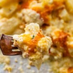 cheesy potatoes on a white plate with lots of cheesy sauce. Bite on a fork ready to eat.