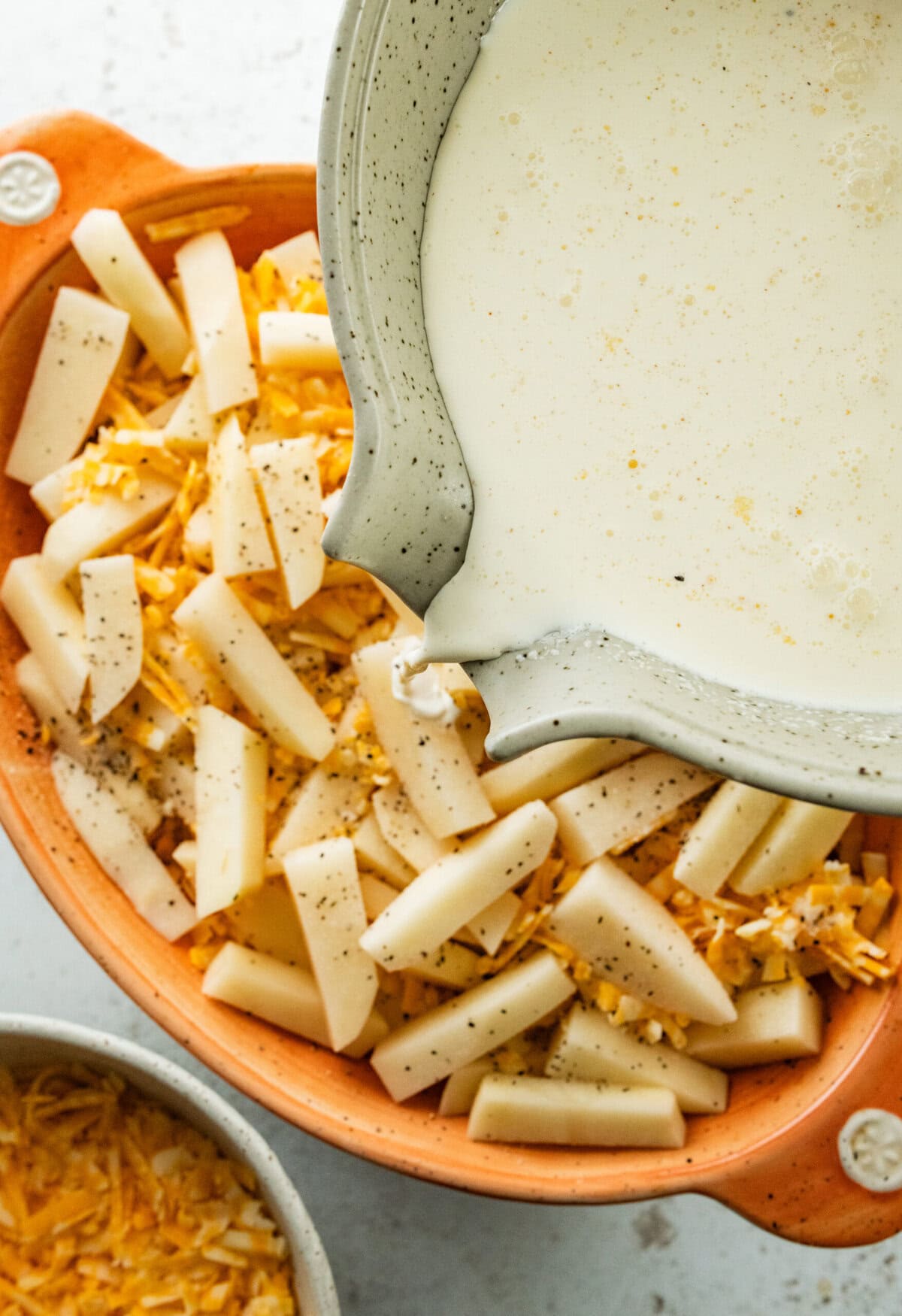 Pouring cream mixture on top of the potatoes and cheese.