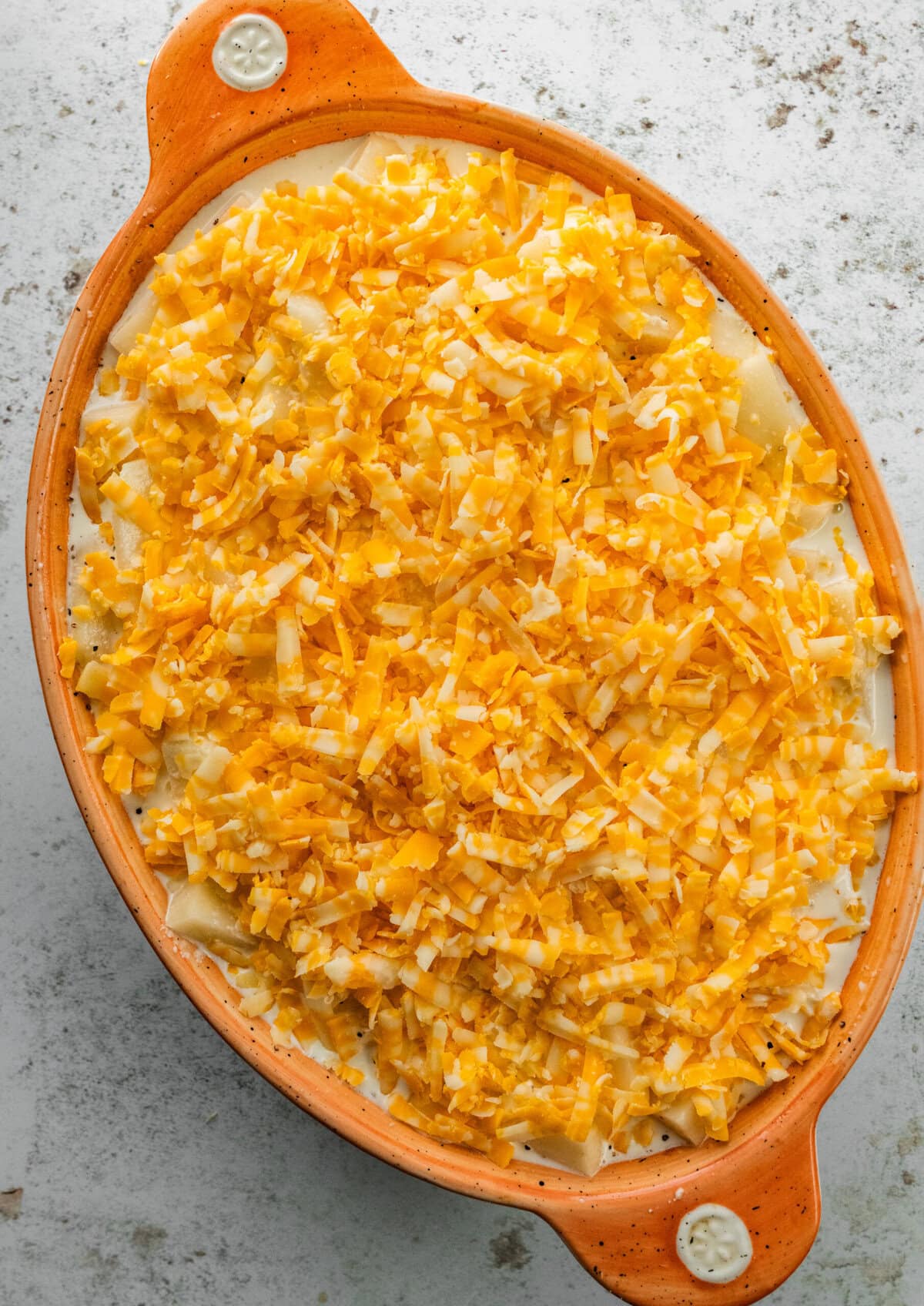 Casserole dish with the easy cheesy potatoes ready to go in the oven with cheese layer on the top.