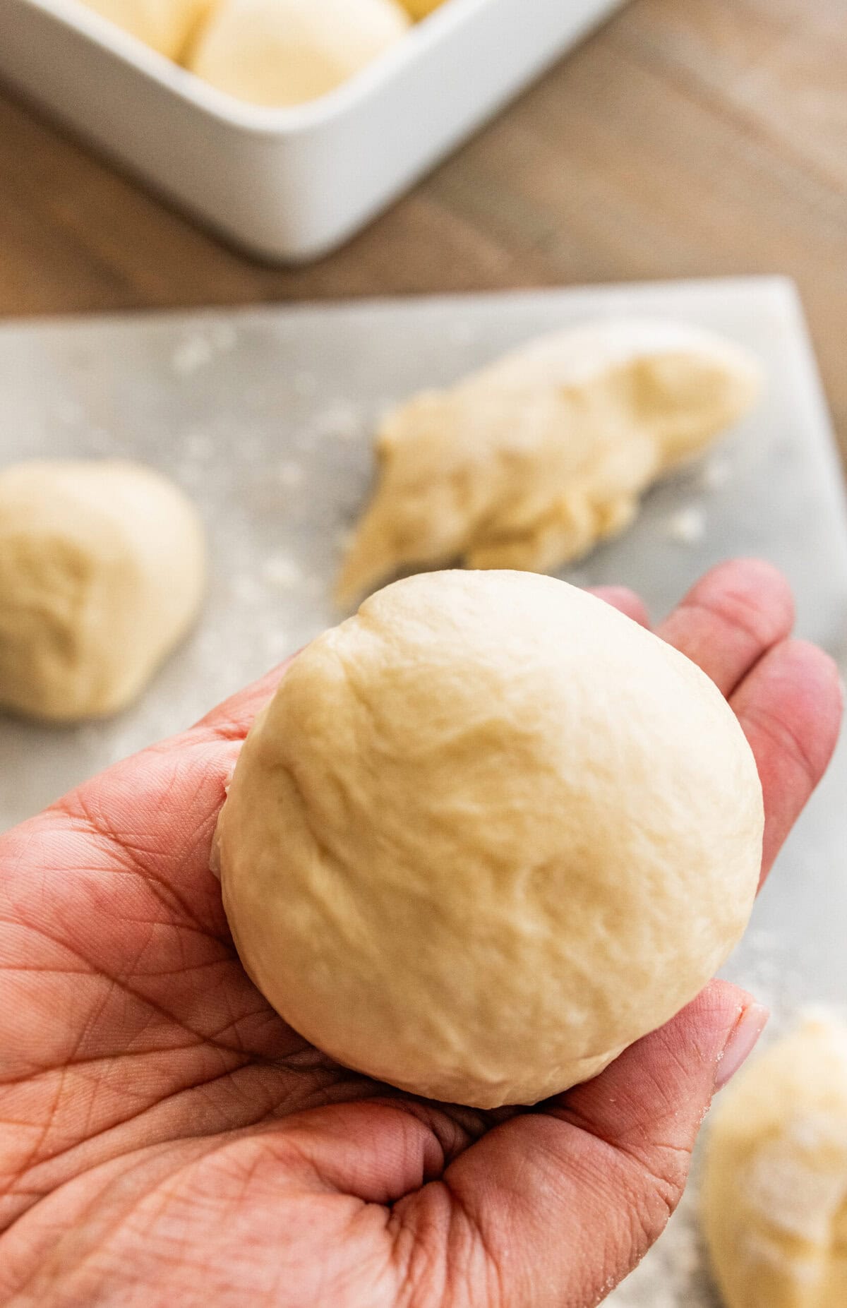 hand holding small dough ball after separating dough into 12 pieces.