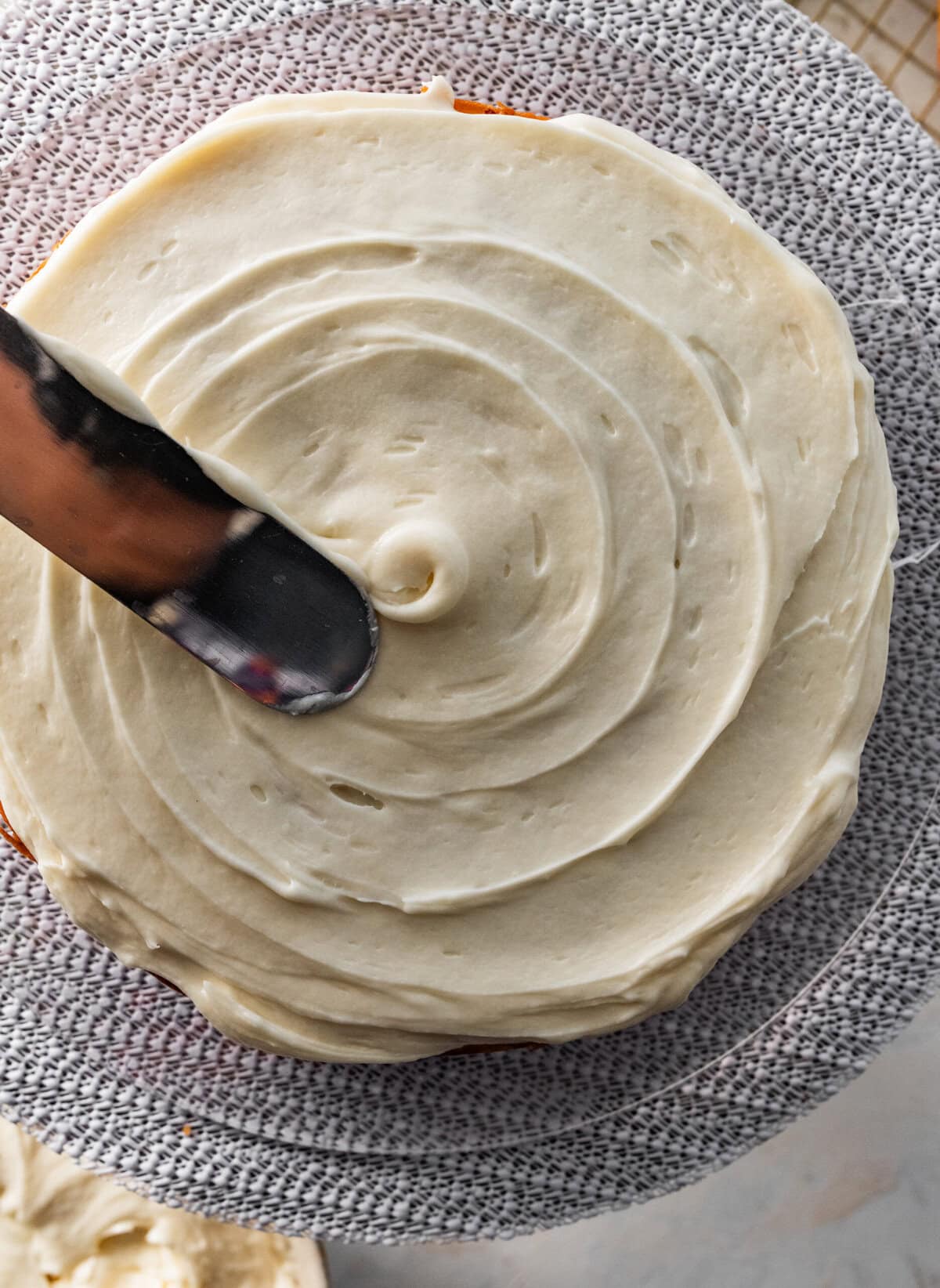 spatula frosting the top of the Italian cream cake in swirl pattern.