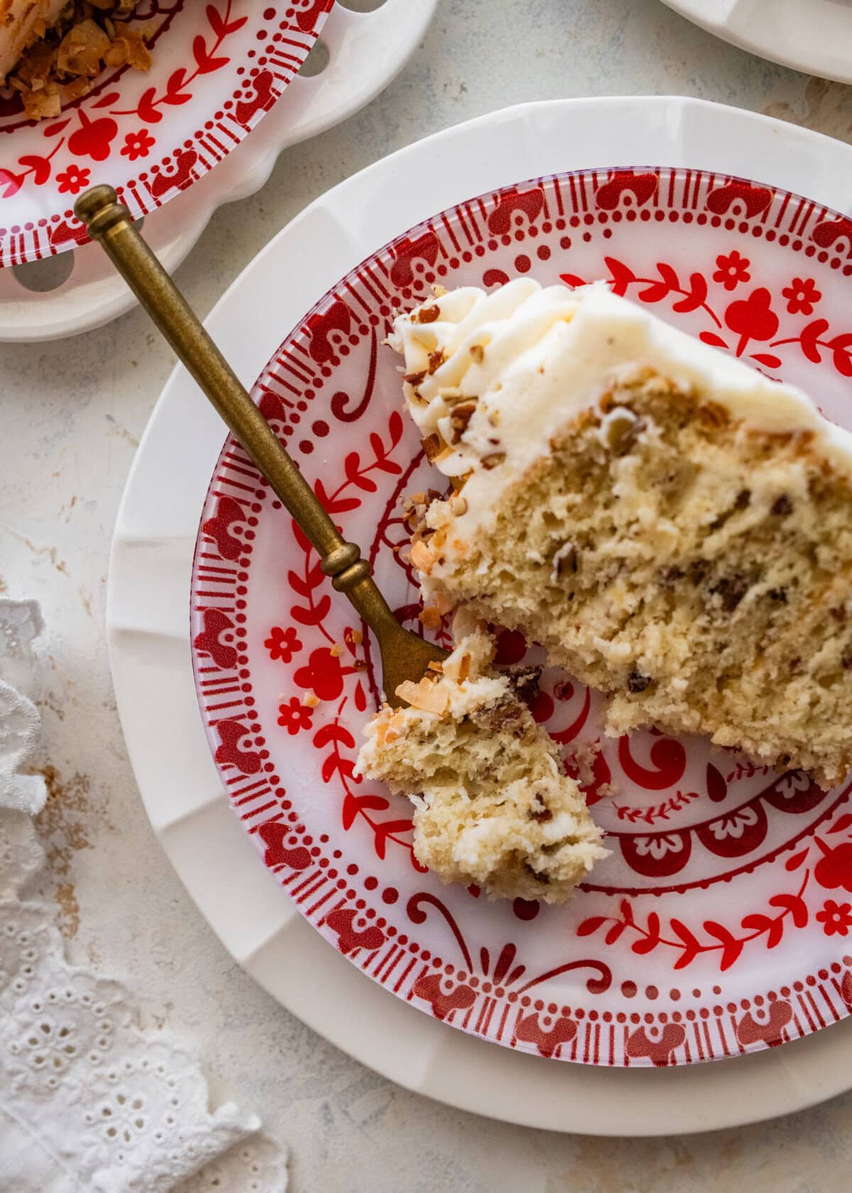 Slice of Italian cream cake on an red and white antique dessert plate. Bite taken out with a fork.
