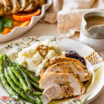 roast turkey breast slices on a plate with mashed potatoes, green beans, and gravy.