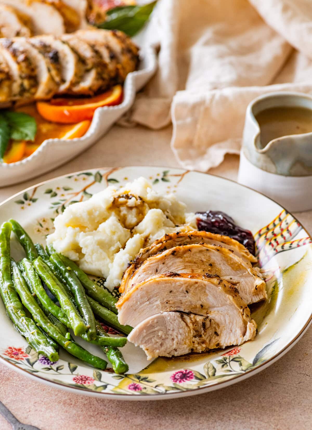 roast turkey breast slices on a plate with mashed potatoes, green beans, and gravy.