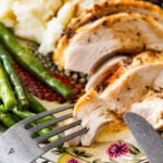 roast turkey breast slices on a plate with mashed potatoes, green beans, and gravy. Fork and knife on plate.