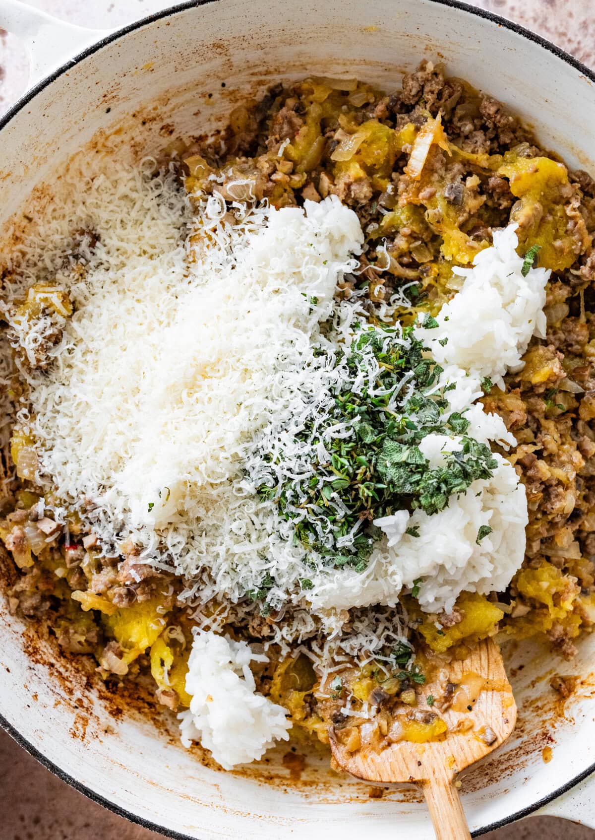 All ingredients for baked acorn squash stuffing including squash and cheese in pan with cooked sausage.