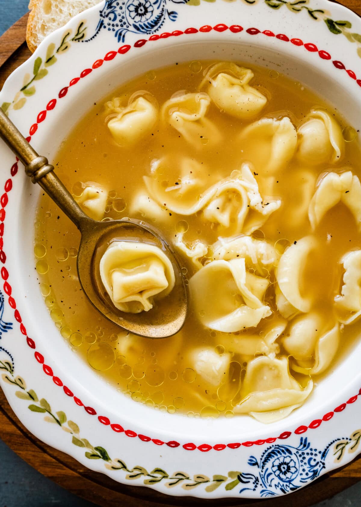 A bowl of tortellini en brodo soup with a spoon lifting up a bite. 