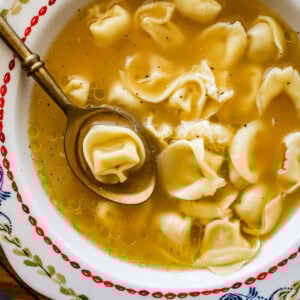 A bowl of tortellini in broth soup with a spoon resting in the dish.