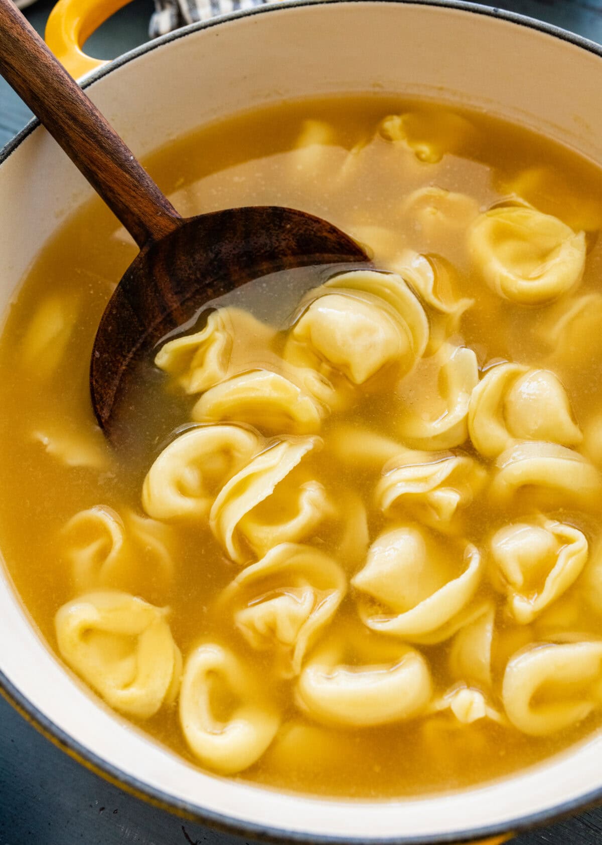 A pot of tortellini brodo soup with a spoon lifting up a portion. 