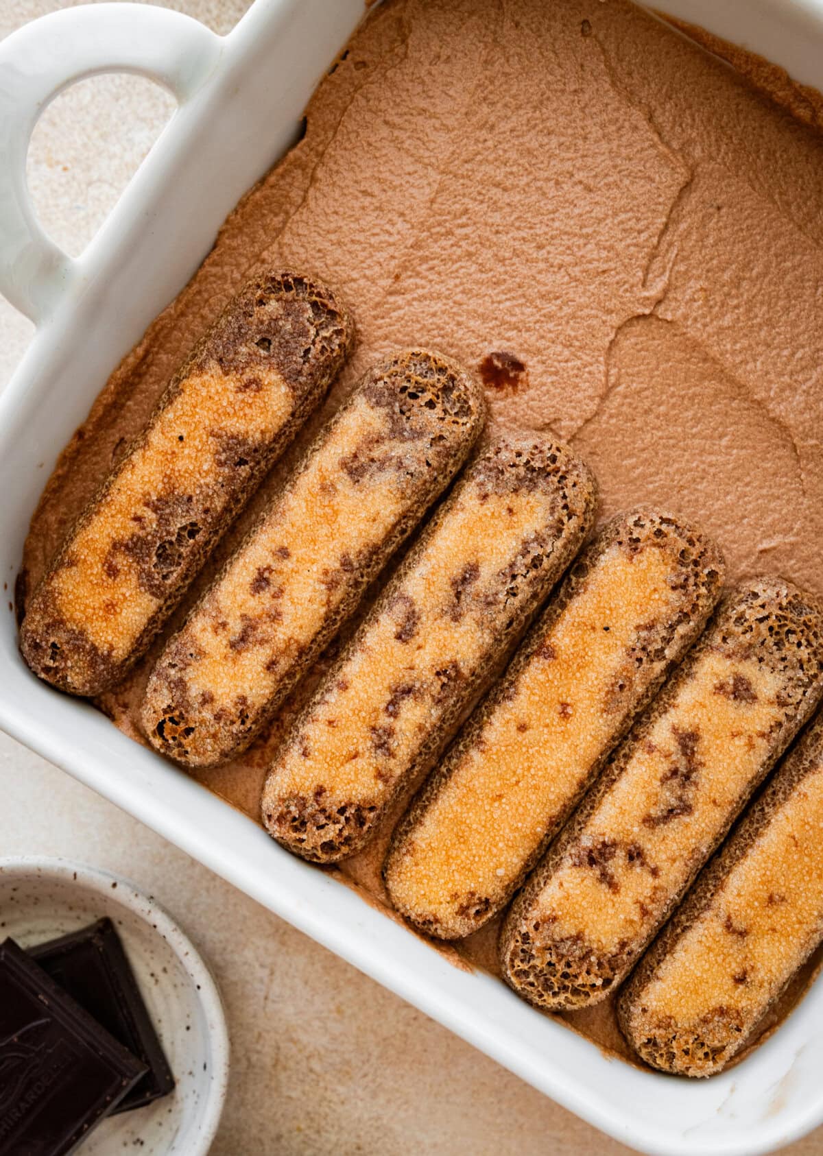 adding another layer of dipped ladyfinger cookies on top of the chocolate custard for the tiramisu.