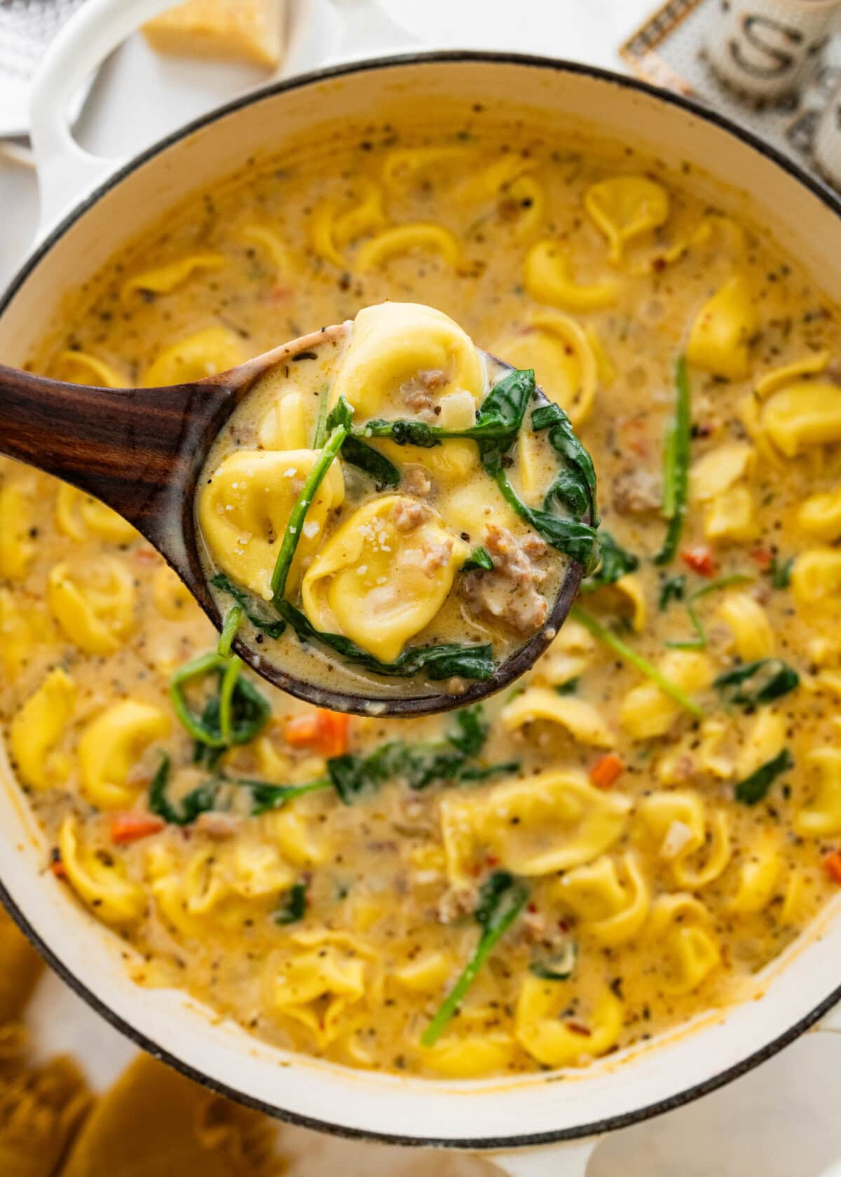 creamy sausage tortellini soup on a pot with a wooden soup spoon in it.