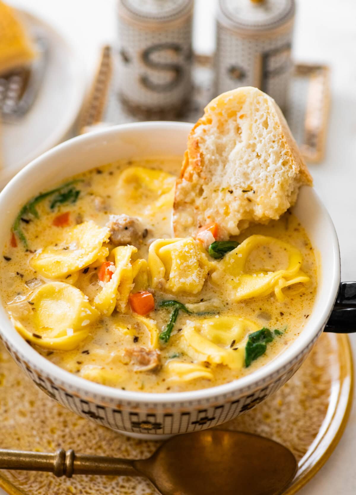 white bowl with creamy sausage tortellini ready to eat. Slice of bread in the bowl.