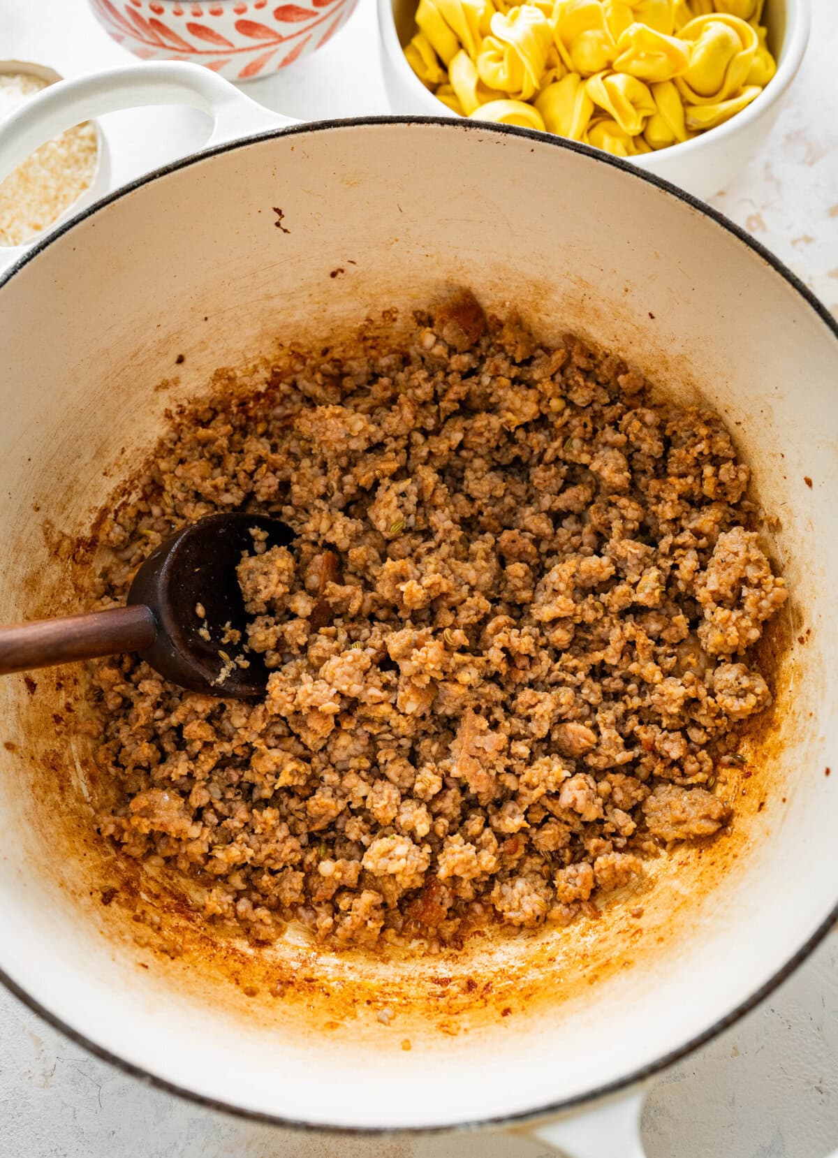 browning sausage in pot with wooden spoon.