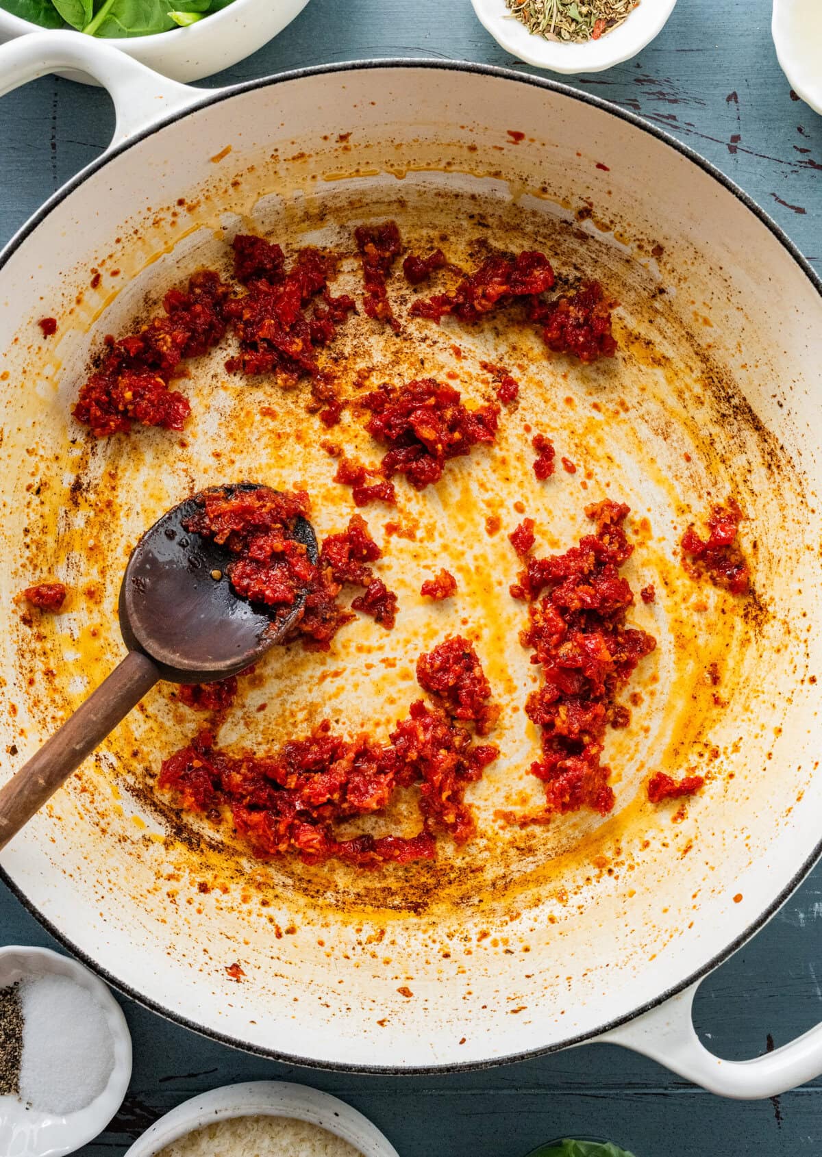 pan with chopped sun dried tomatoes and a wooden spoon.