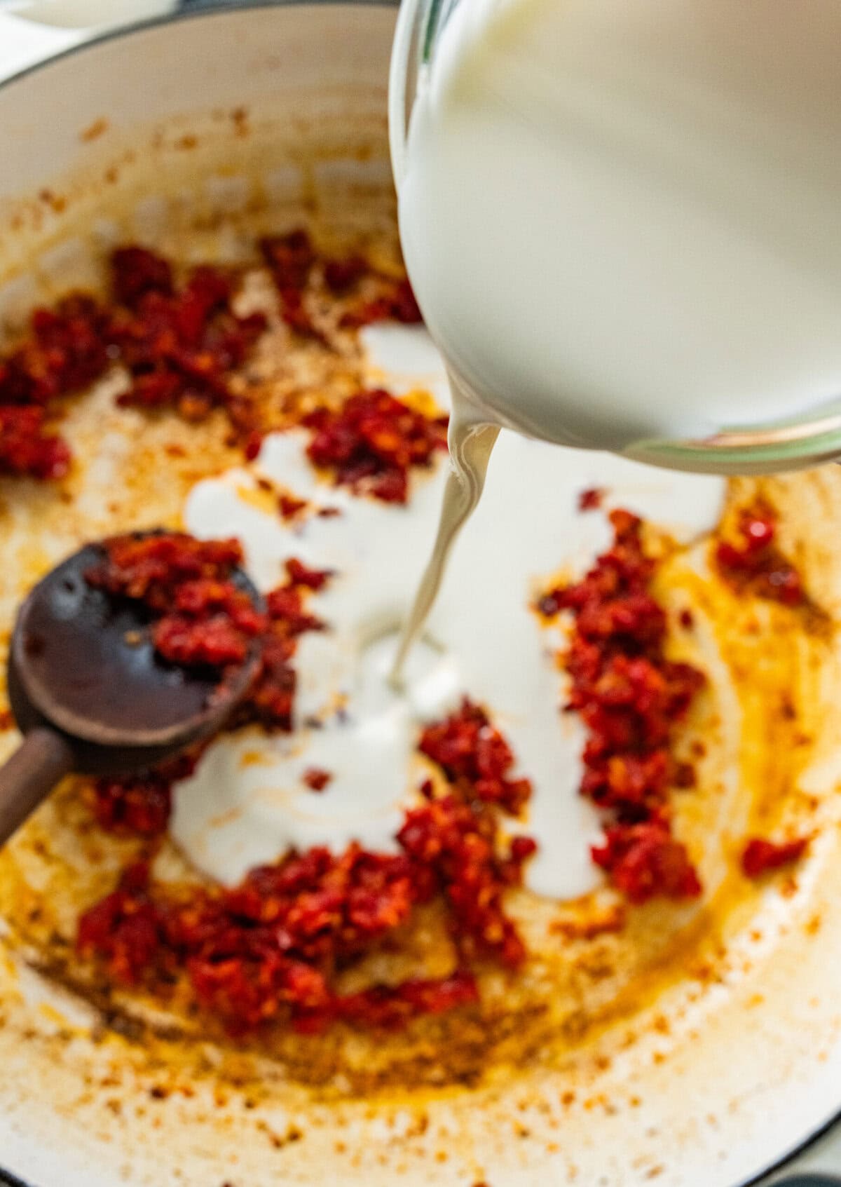 cream being poured into pan with sun dried tomatoes.