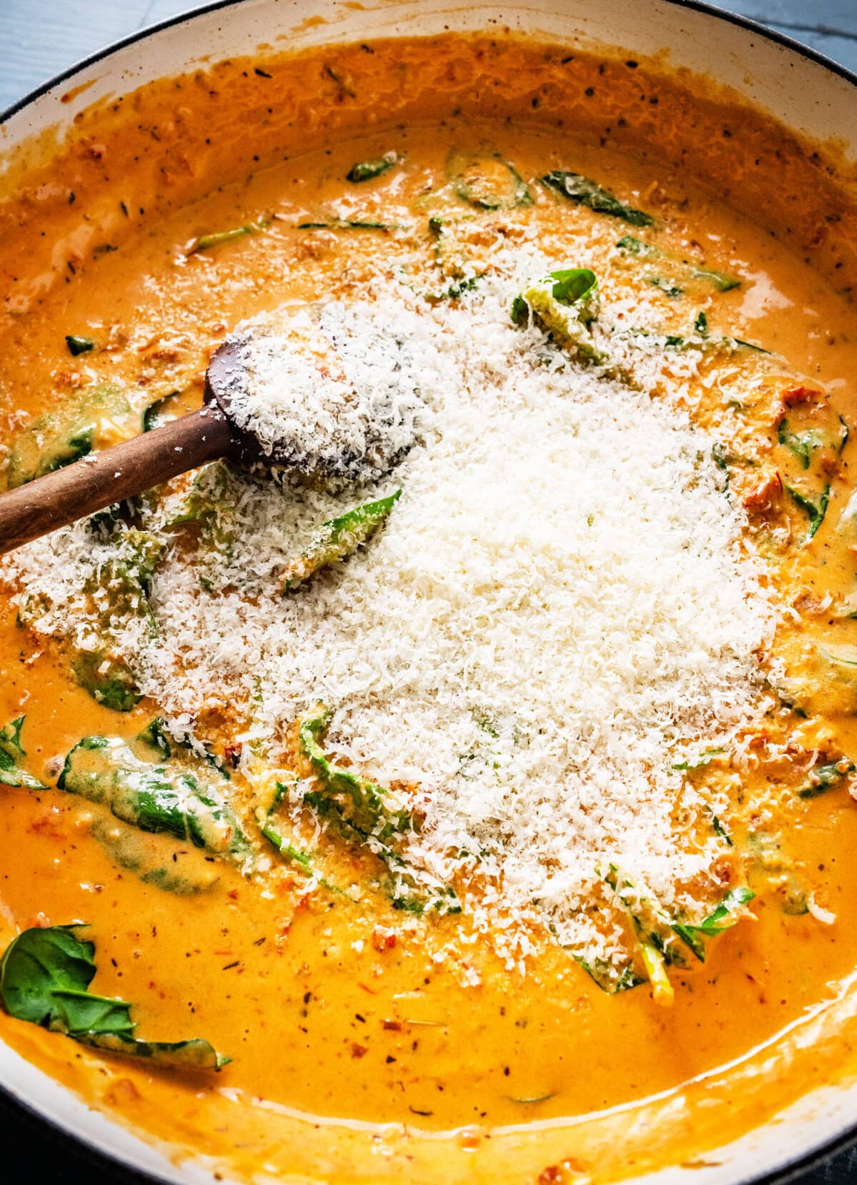creamy sun dried tomatoes sauce in a pan with spinach and parmigiano cheese.