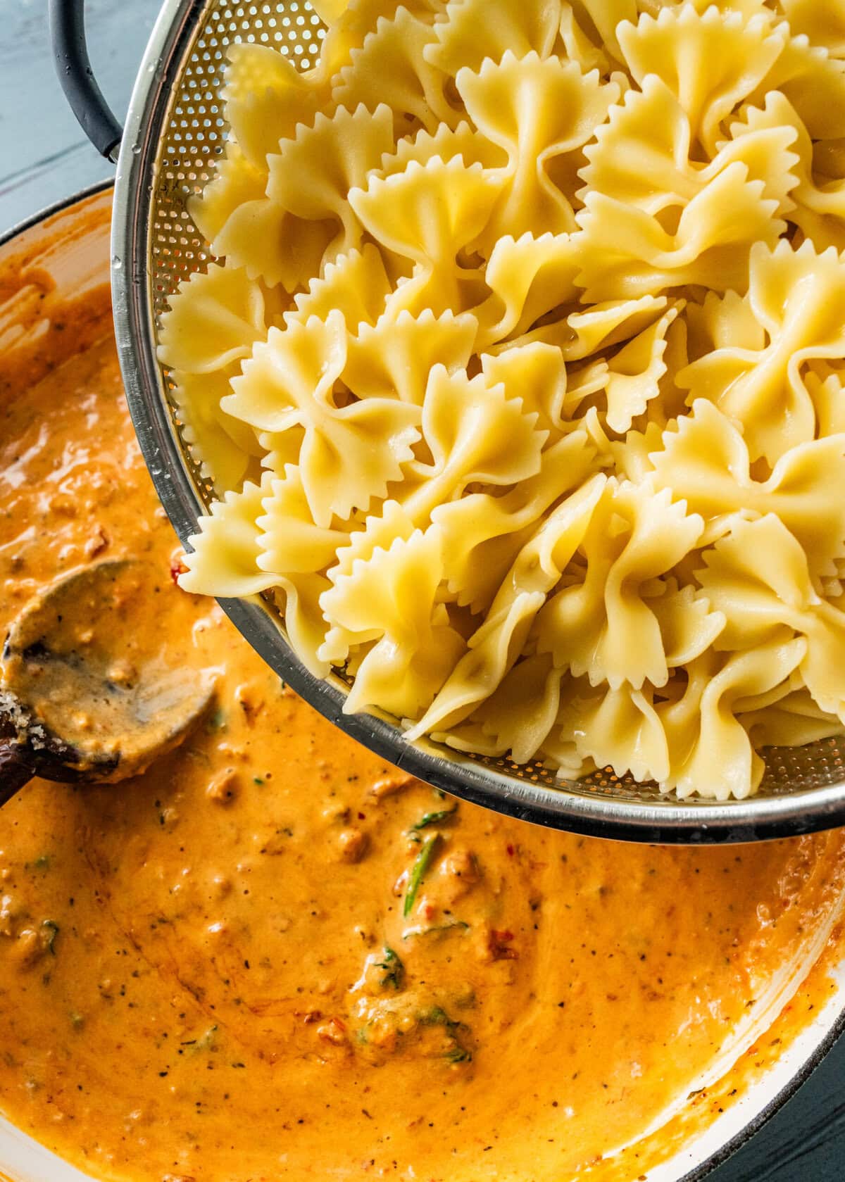 cooked bow tie pasta poured into the pot with creamy sundried tomato sauce.