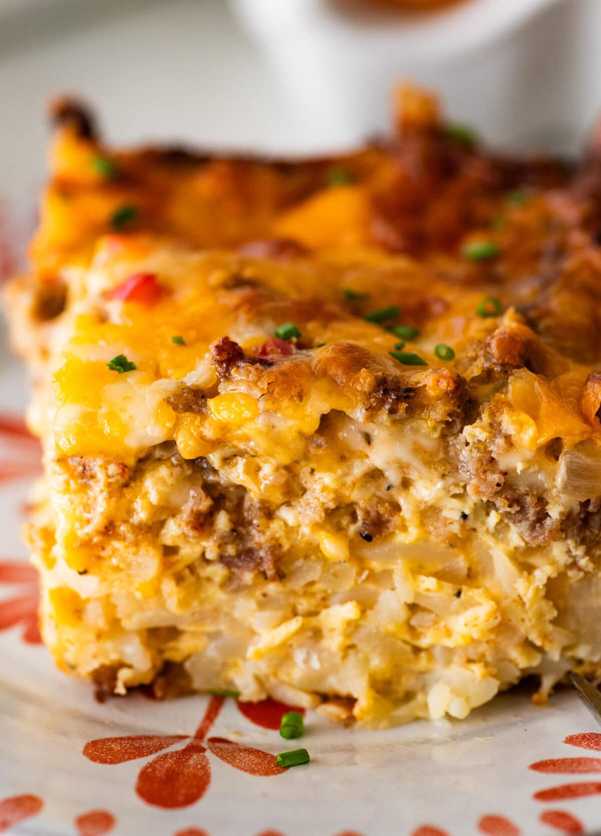 one piece of the hashbrown breakfast casserole on a plate with a fork by it. Gooey cheese and meats.