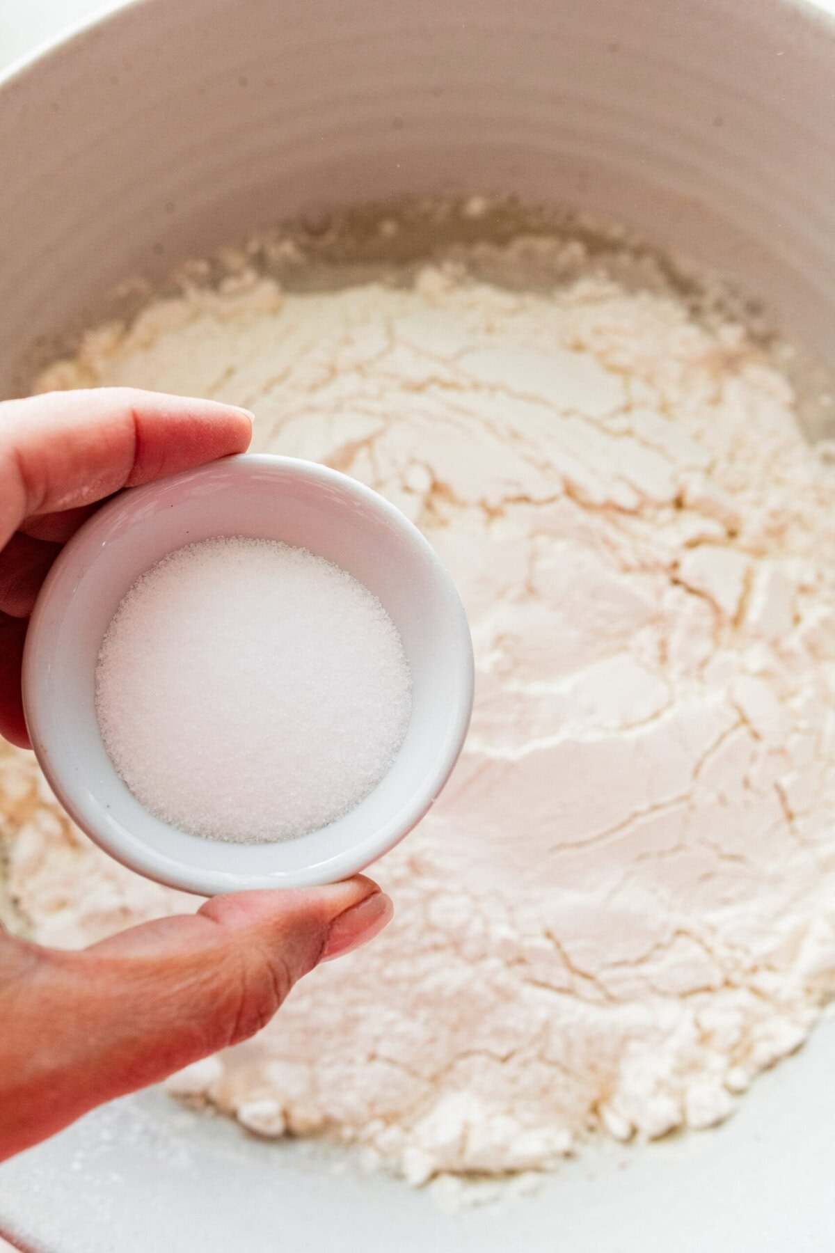 Flour added to the bowl and a hand holding the salt above. 