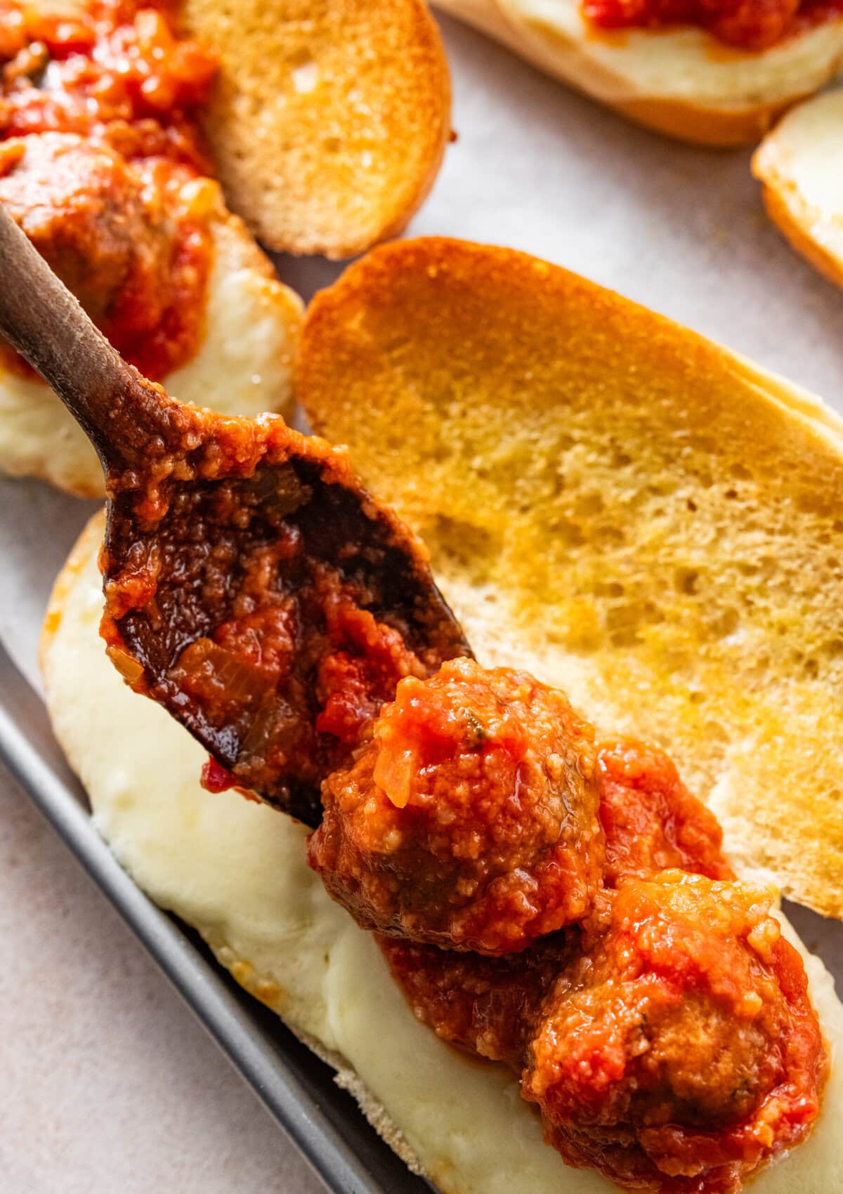 spoon adding the meatballs and sauce to a toasted roll with melted cheese.