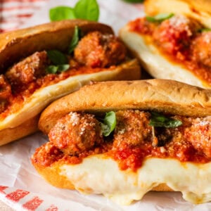 Italian meatball subs on a platter with gooey cheese on the side of subs.