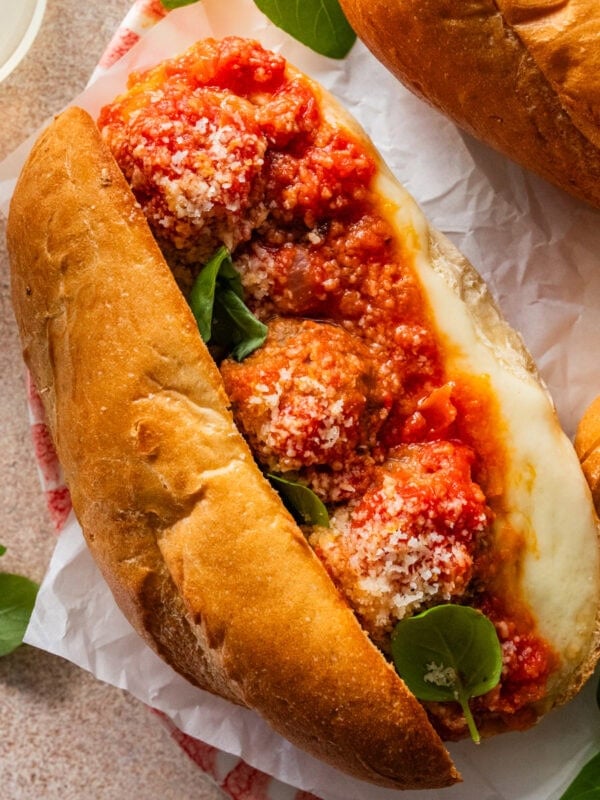 Italian meatball subs on a platter with gooey cheese on the side of subs.