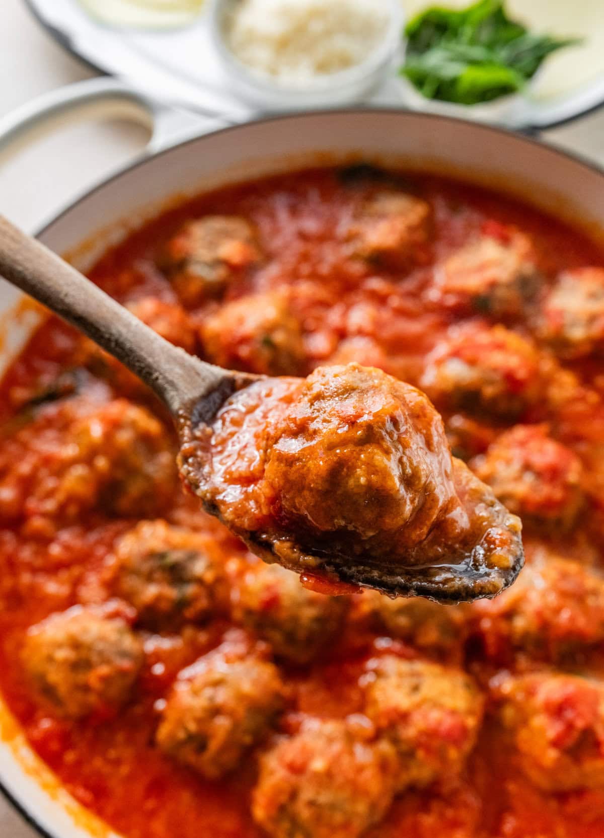 cooked meatballs in a pan with wooden spoon holding one.