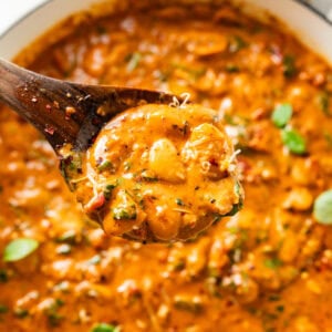 pot of creamy marry me butter beans with a wooden spoon holding some to serve.