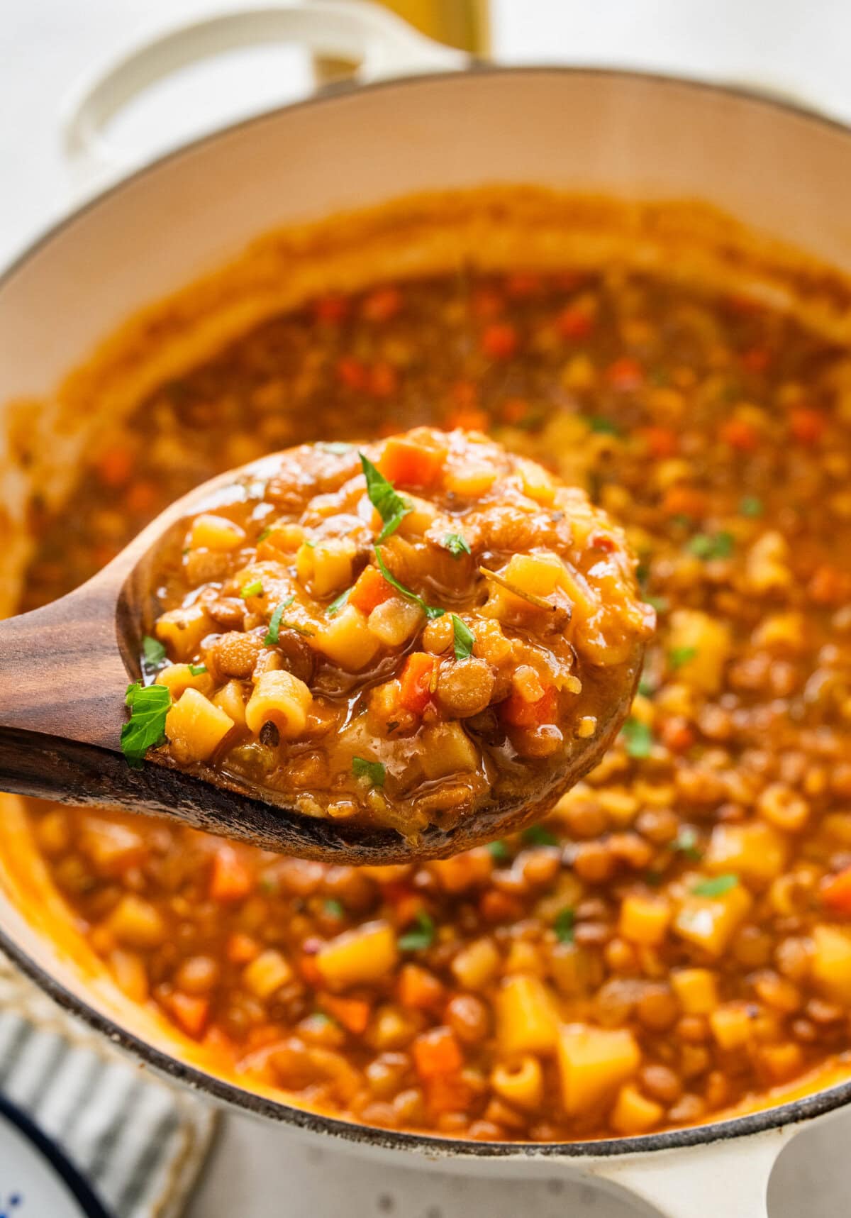 wooden ladle in pot with cooked lentils and veggies.