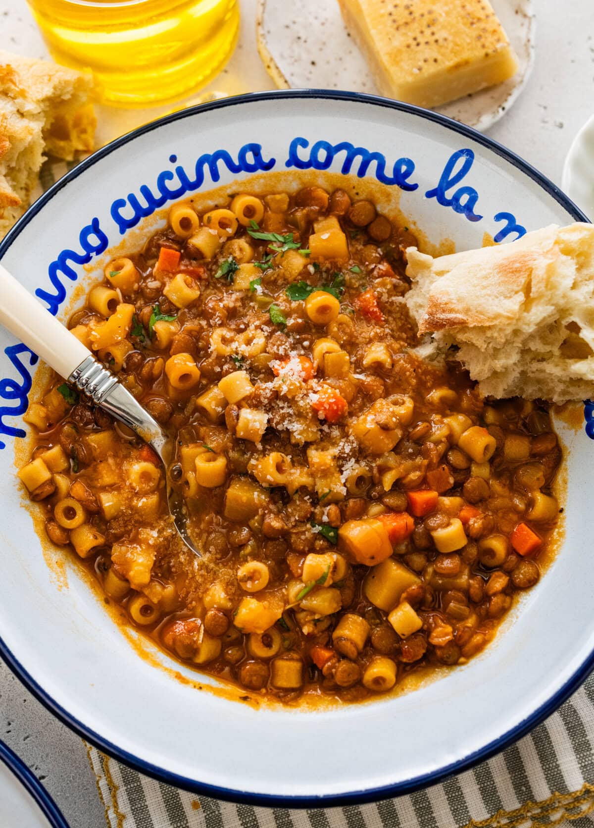 Italian bowl with cooked lentils and pasta in it with a spoon. Crusty bread on the side.