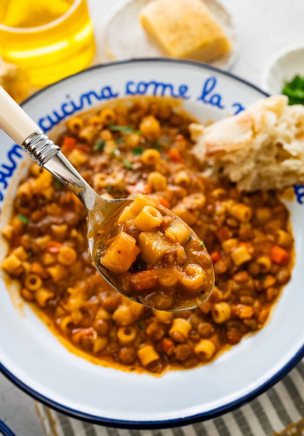 Italian bowl with cooked lentils and pasta in it with a spoon. Crusty bread on the side.