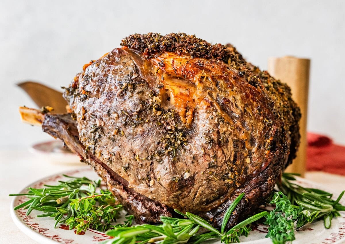 standing prime rib roast recipe on a platter with herbs around it.
