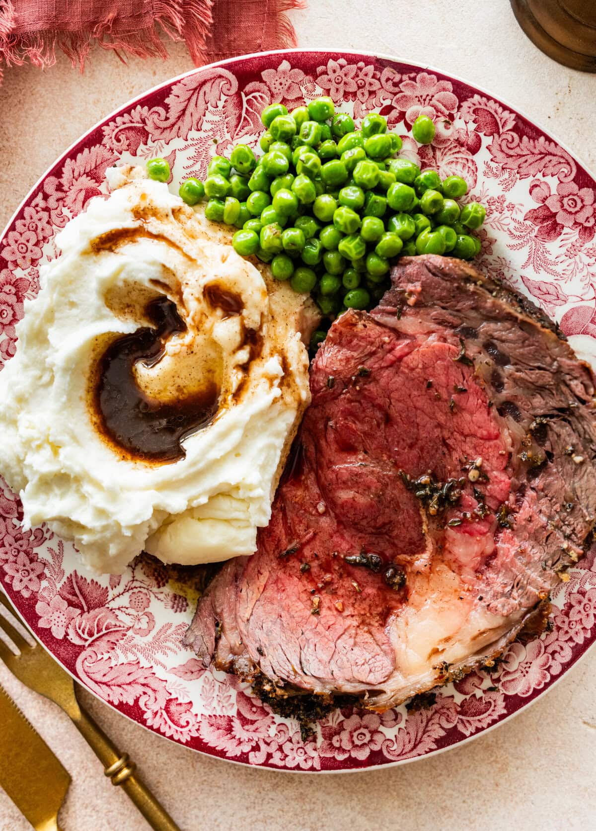 festive plate with a slice of prime rib roast meat, peas, mashed potatoes, and gravy.