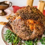 standing prime rib roast recipe on a platter with herbs around it.