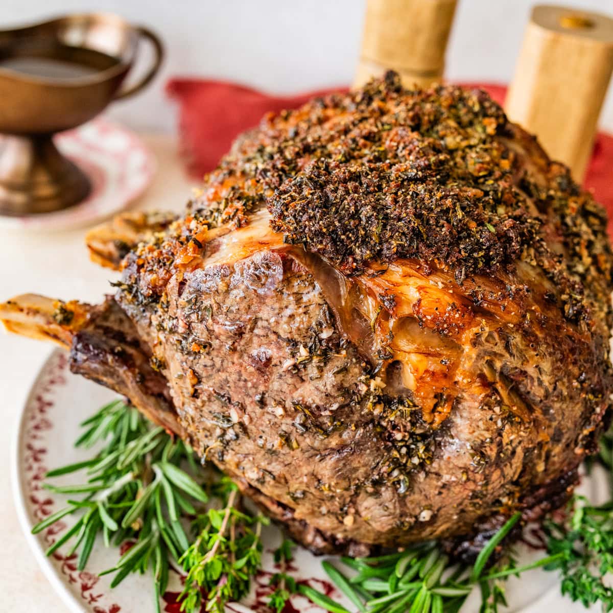 standing prime rib roast recipe on a platter with herbs around it.