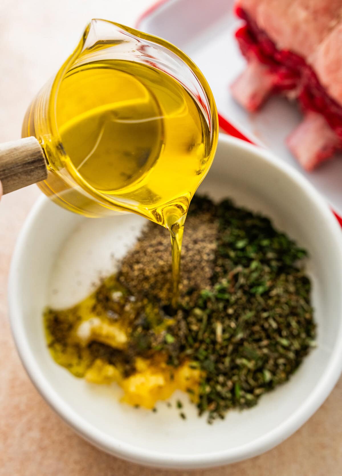 pouring olive oil into bowl with herbs for the meat marinade.